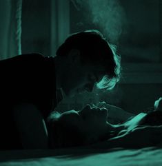 a man and woman laying on a bed in the dark