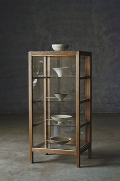 a display case with glass doors and plates in the bottom section, on concrete flooring