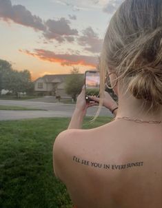 a woman with a tattoo on her back taking a selfie in front of the sunset