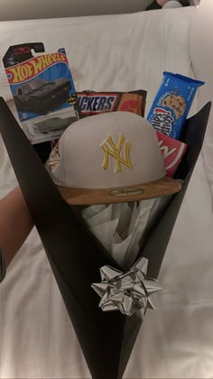 a baseball cap and other items are placed in a black box on a bed with white sheets