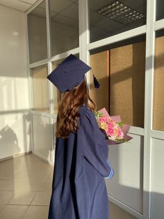 a woman in a graduation gown and cap is looking out the window while holding flowers