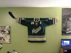 a hockey jersey hanging on the wall in a room with a laptop and other items