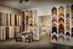 a room filled with lots of different colored rugs on the wall next to two chairs