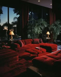 a living room filled with lots of red couches next to tall windows at night