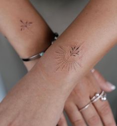 two hands holding each other with small tattoos on their arm and wrist, one has a sunburst in the middle