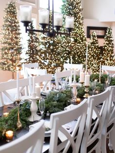 a dining room table set for christmas with candles and greenery on the centerpiece