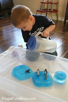 a young boy is playing with penguins in an ice cream container and water jugs