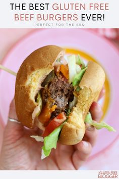 a hand holding a sandwich with meat, lettuce and tomato on it in front of a pink plate