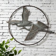 two birds are flying in the air on a circular metal wall decoration with white brick background