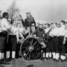 an old black and white photo shows people standing around a baby carriage, with one person sitting on the ground