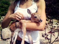 a woman holding a baby deer in her arms