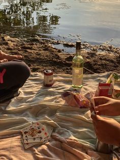 a person sitting on the sand with some food and drinks in front of them,