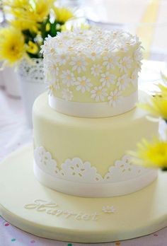 a three tiered cake sitting on top of a table next to some yellow flowers