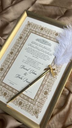 a wedding card with a feather resting on it's side next to a pen