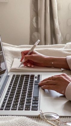 a woman is writing on her notebook while sitting in front of an open laptop computer