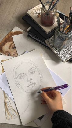 a6b7cfd6-7b3e-4f7e-b488-ca3a4957e0dc Artist's hand sketching a female portrait, surrounded by art supplies and sketches on a wooden desk. | Sky Rye Design