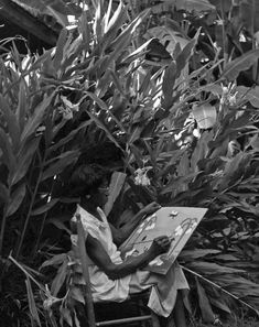 a woman sitting in a chair with a painting on it's easel next to some plants