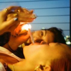 two women are sharing a drink and cake with one another while the other holds a lit candle in her mouth