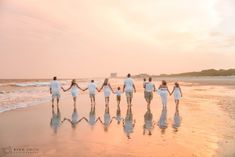 a group of people holding hands walking on the beach at sunset or sunrise with their reflection in the wet sand