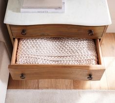 an open drawer on the side of a bed with a white blanket in it and a book