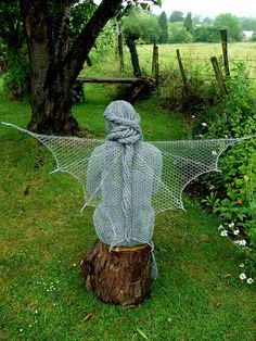 a scarecrow statue sitting on top of a tree stump in the grass next to a fence