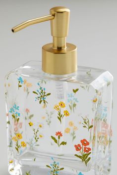 a glass soap dispenser with flowers painted on the front and gold faucet