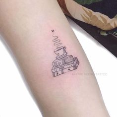 a woman's arm with a stack of books and a coffee cup tattoo on it