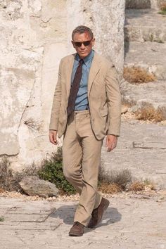 a man in a tan suit and tie walking down the street with his hands in his pockets