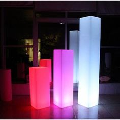 three tall white and pink lights are lit up at night in front of a building