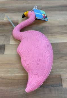 a pink flamingo sitting on top of a wooden floor next to a card holder