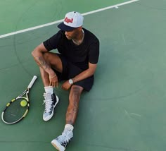 a man sitting on top of a tennis court with a racquet next to him