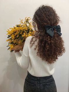 a woman with long curly hair wearing a white sweater and holding a bouquet of yellow flowers