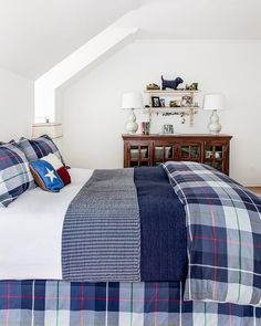 a bed with plaid sheets and pillows in a white room next to a wooden dresser