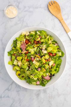 a white bowl filled with lettuce and meat next to a wooden utensil