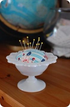 a small white bowl with pins in it on a wooden table next to a globe