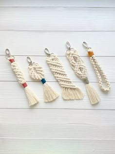 four tasselled key chains hanging from hooks on a white wooden background with text overlay