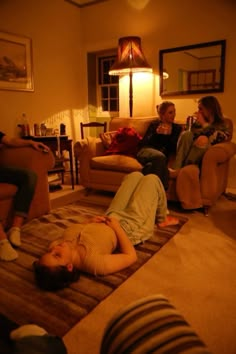 three people are sitting in a living room and one person is laying on the floor