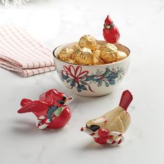 three small ceramic birds sitting next to a bowl filled with gold foiled chocolates