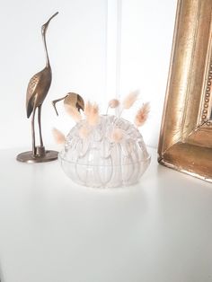 there is a glass bowl with feathers in it and a bird statue next to it