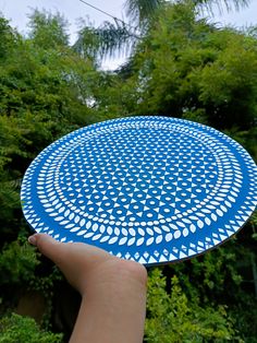 a hand holding a blue and white frisbee in front of trees