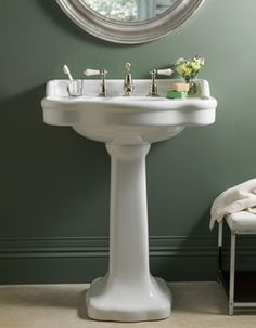 a white pedestal sink sitting under a round mirror