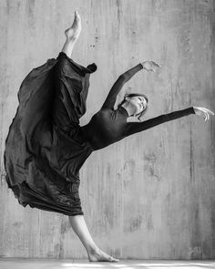 black and white photo of a woman dancing in front of a concrete wall with her arms stretched out