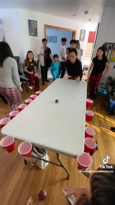 a group of people standing around a table with red cups on it and one person holding a cell phone