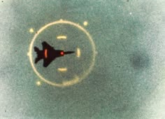 a fighter jet flying through the sky in front of a circular white circle with an orange tail