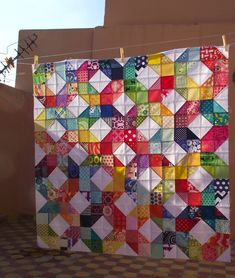 a multicolored quilt hanging on a clothesline in front of a building with a tiled floor