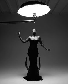 a woman in a long black dress is standing under a light with her hands out