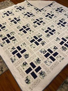 a white quilt with black squares and flowers on the bottom is laying on a wooden floor