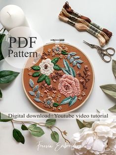 an embroidery pattern with flowers and leaves on the hoop next to scissors, thread, and other crafting supplies