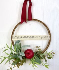 a wreath hanging on the side of a wall with two apples and greenery around it