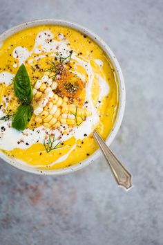 a white bowl filled with yellow soup and garnished with herbs